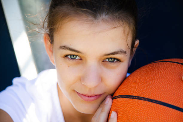 Portrait of a beautiful and young female basketball player with face resting on the ball