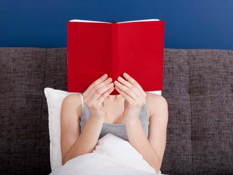 Woman reading a book with the face covered by the book