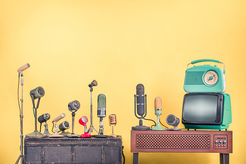 Retro microphones for interview or press conference, old mint green TV set and radio from 60s front yellow wall background. Vintage style filtered photo