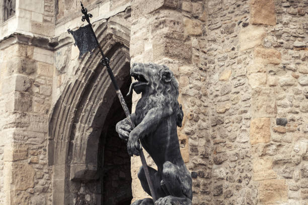 Statue of a lion putting a paw on a ball. Classical marble lion sculpture close-up outdoor. Face of a ferocious lion with open mouth.