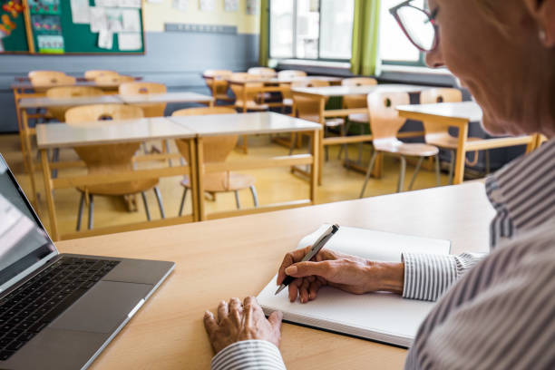 insegnante matura che scrive note nel suo taccuino in classe. - grading teacher desk writing foto e immagini stock