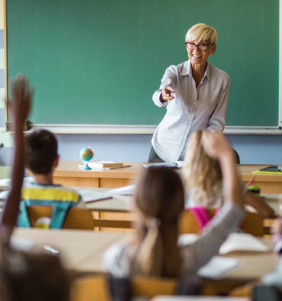 istock Happy mature elementary teacher aiming at school kids to answer her question. 1157341725
