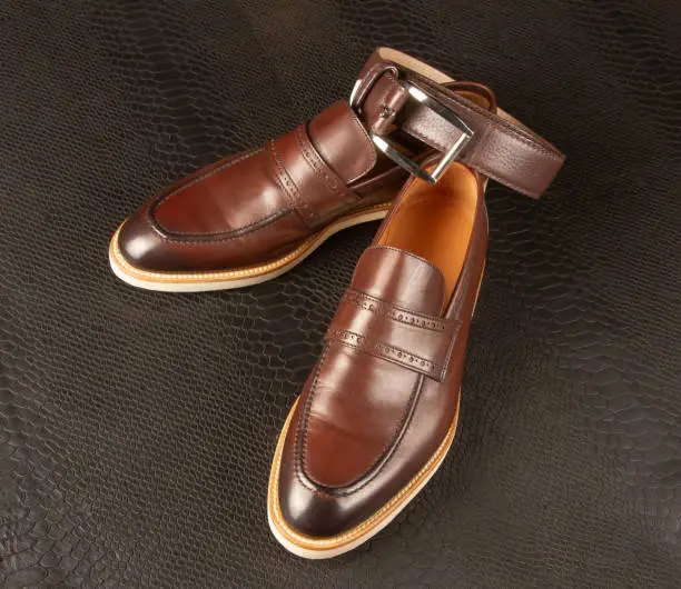 Photo of Brown men's shoes with light soles and a belt against the background of python leather