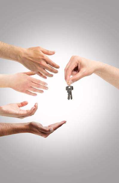 Studio shot of unidentifiable hands reaching for a set of keys against a gray and white background