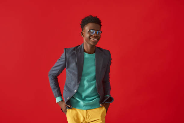 istock Smiling Afro American guy in stylish clothes posing on red background 1157343624