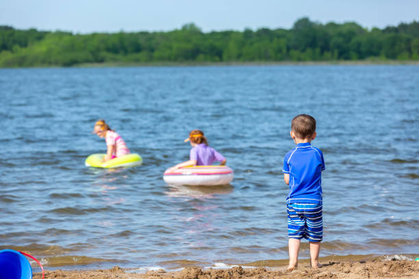 istock Young Boy At Beach Watching Sisters In the Water 1157345402