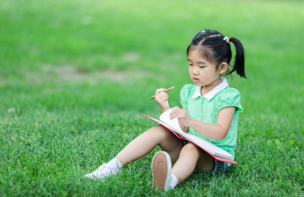 istock Cute Little girl sitting on the grass studying 1157351233