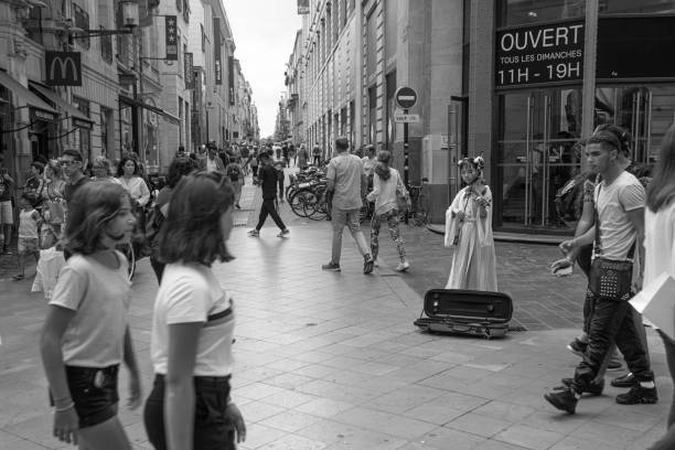 A Japanese violinist busking in the centre of Bordeaux, France. There are people walking in the foreground with the Shops and restaurants in the background.