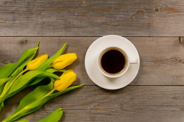 Yellow tulips and coffee cup on rustic wooden table. Top view with copy space.