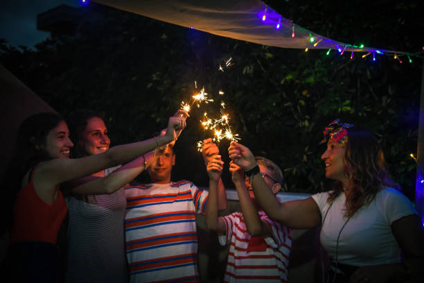 gruppe von verschiedenen personen, die party mit feuerwerk im freien auf der terrasse. lächelnde mädchen und jungen, die spaßig zusammen genießen funkelnden familiengeburtstag. jugendglück und urlaubskonzept - sparkler sparks new years eve human hand stock-fotos und bilder