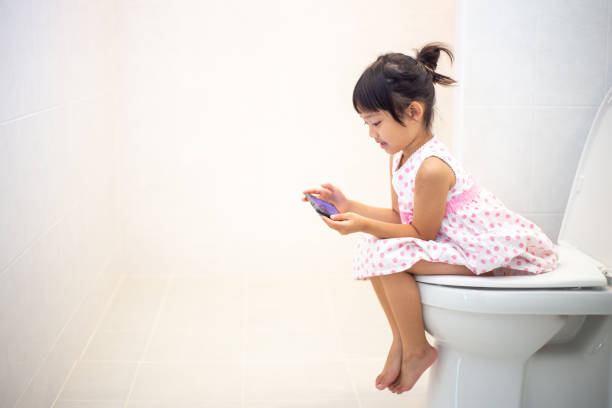 asian children sitting on a toilet and holding smartphone. asian children sitting on a toilet and holding smartphone. potty toilet child bathroom stock pictures, royalty-free photos & images