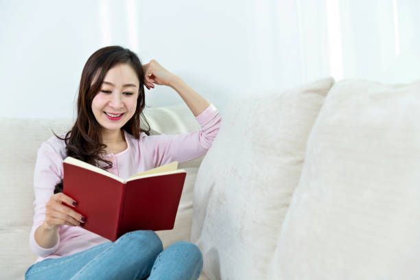 istock Beautiful woman sitting on sofa reading book 1157371180