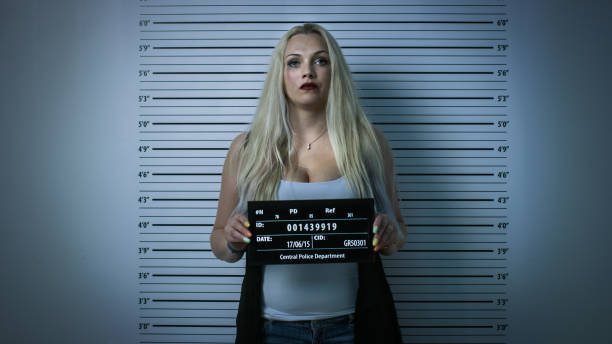 In Police Station Arrested Woman Posing for Front-View Mugshot. Wears Saucy Clothes, Has Smudged Heavy Makeup, Her Hair Is Disheveled and She Holds Placard. Height Chart in Background. Vignette Filter In Police Station Arrested Woman Posing for Front-View Mugshot. Wears Saucy Clothes, Has Smudged Heavy Makeup, Her Hair Is Disheveled and She Holds Placard. Height Chart in Background. Vignette Filter arrest photos stock pictures, royalty-free photos & images