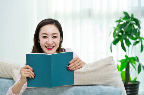 istock Beautiful woman lying on the sofa reading book 1157372741