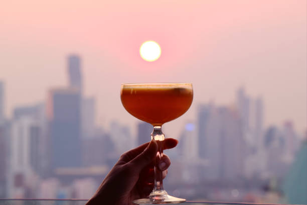 Woman's hand holding a cocktail glass against the setting sun with blurry skyscrapers in background