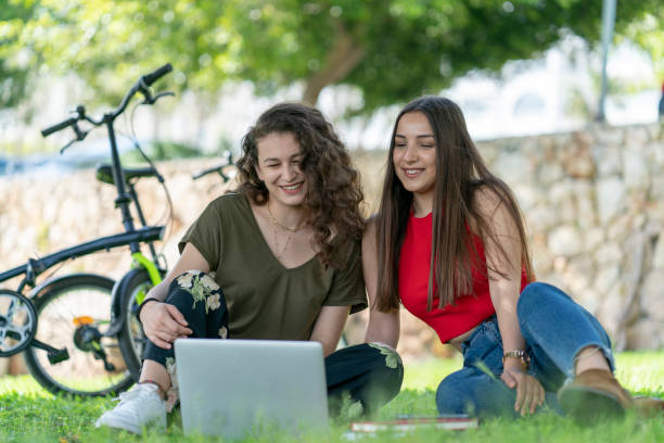 istock Happy and smiling two female student friends lying down on the grass in the park while using a laptop together. 1157374351