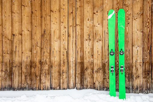 grean back counry skis with technical bindings leaning on wooden wall