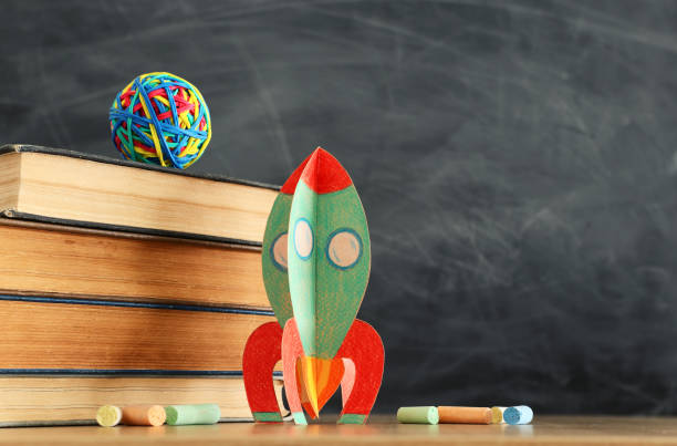 istock education and back to school concept. cardboard rocket, books and chalks in front of classroom blackboard 1157382803