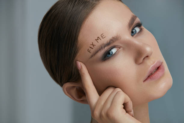 Beauty makeup. Woman face with messy eyebrow and fix me on skin Beauty makeup. Woman face with messy eyebrow and fix me sign on skin closeup. Girl model with bushy fluffy messed up eyebrows and words written above. Eyebrow correction concept bushy stock pictures, royalty-free photos & images