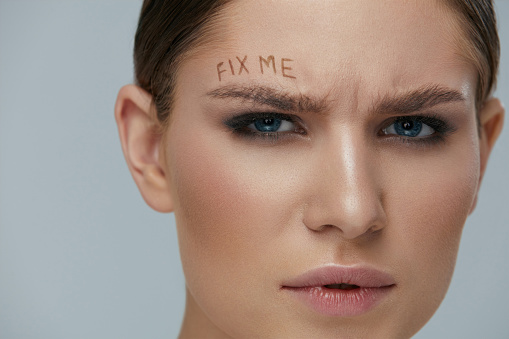 Beauty makeup. Woman face with messy eyebrow and fix me sign on skin closeup. Girl model with bushy fluffy messed up eyebrows and words written above. Eyebrow correction concept
