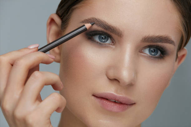 maquillaje de belleza. mujer dando forma a la ceja con el primer plano del lápiz de la ceja - makeup pencils fotografías e imágenes de stock