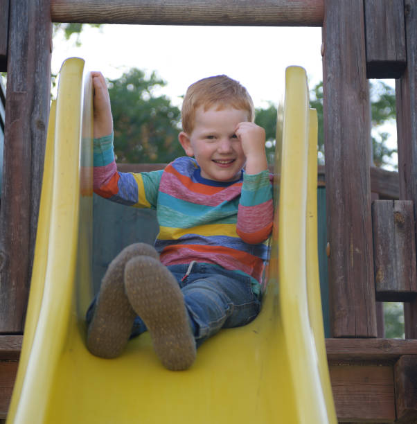 istock 5 years old redheaded happy boy sits on a slide and smiling 1157388784