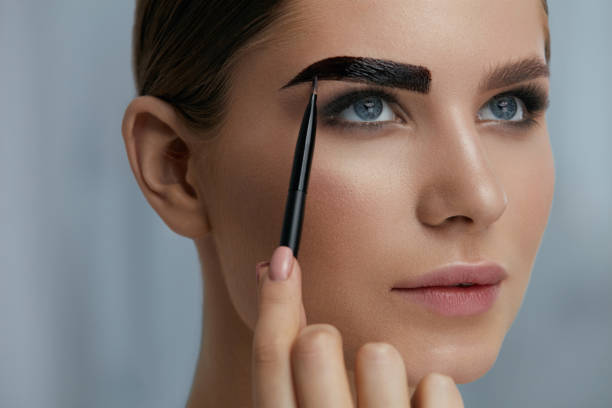 Eyebrow coloring. Woman applying brow tint with makeup brush Eyebrow coloring. Woman applying brow tint with makeup brush closeup. Girl model using liquid peel-off brow gel, beauty product on eyebrows hand tinted stock pictures, royalty-free photos & images