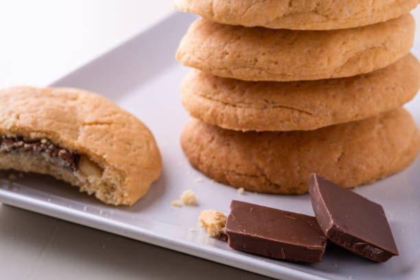 istock Homemade stack of shortbread chocolate cookies with one bitten cookie and two pieces of chocolate on white plate wooden table 1157390592