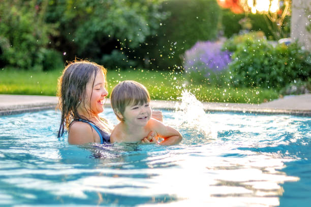 happy siblings playing in swimming pool outdoors in garden. preteen sister teaching her little brother to swim. summer holidays lifestyle and leisure activity. - swimming child swimwear little boys imagens e fotografias de stock