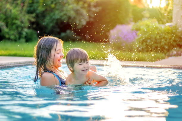 happy siblings playing in swimming pool outdoors in garden. preteen sister teaching her little brother to swim. summer holidays lifestyle and leisure activity. - swimming child swimwear little boys imagens e fotografias de stock