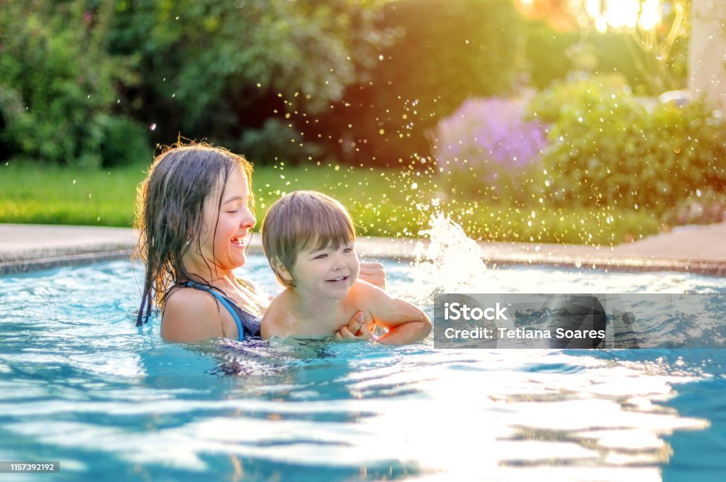 Lyckliga syskon leker i poolen utomhus i trädgården. Preteen syster lära sin lillebror att simma. Sommarlov livsstil och fritids aktiviteter. - Royaltyfri Simbassäng Bildbanksbilder