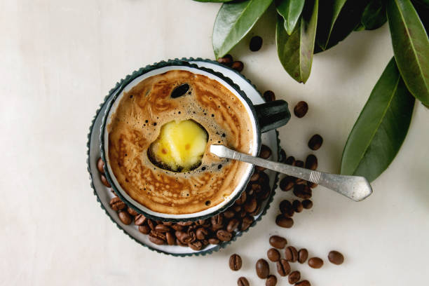 Bulletproof coffee with butter Bulletproof coffee. Keto diet coffee in blue ceramic cup with organic ghee butter in spoon inside with beans and green branch over white marble background. Flat lay, space ghee stock pictures, royalty-free photos & images