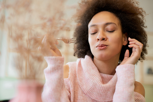 Portrait of charming positive mixed race woman in pink turtleneck sweater sitting in confectionery and eating gateau.