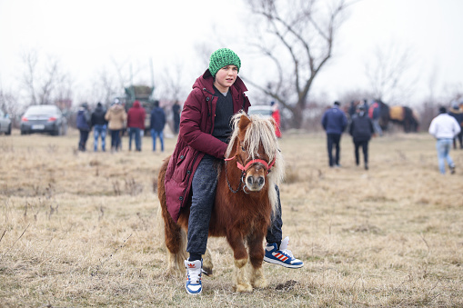Pietrosani, Romania - January 6, 2019: Young boy is bareback riding a pony before an Epiphany celebration horse race.