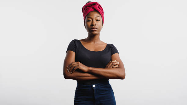 African woman in headwrap African female with a cloth wrapped on head looking at camera. Portrait of african woman standing with her arms crossed isolated on white background. turban stock pictures, royalty-free photos & images