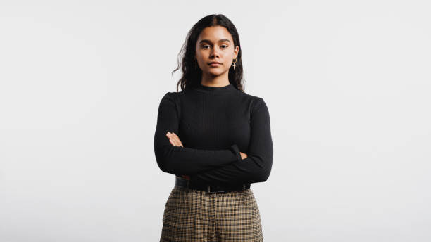 Portrait of young woman Portrait of young woman looking at camera. Woman standing against white background with her arms crossed. grave stock pictures, royalty-free photos & images