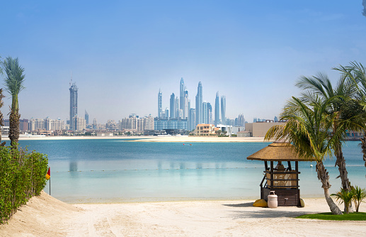 Dubai, UAE, United Arab Emirates - 28 May, 2019: Palm Jumeirah beach with white sand. Skyscrapers of Dubai Marina at the distance
