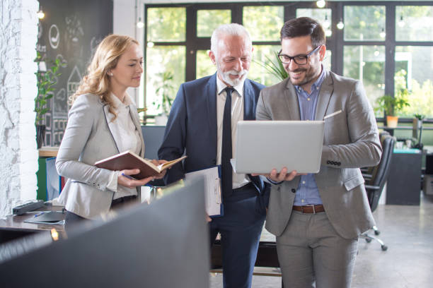 istock Group of three business people looking something on laptop while standing in modern office 1157433914