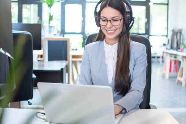 istock Smiling young business woman with headset using laptop in office 1157435079