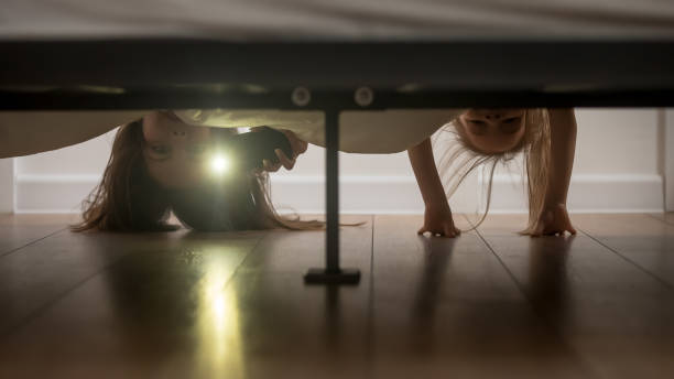 Mother and daughter shine a flashlight looking under the bed Mother and daughter, babysitter and kid girl afraid of monsters hold smartphone shine a flashlight under the bed looking on floor check ghosts, older younger sisters playing having fun at home concept funny shock stock pictures, royalty-free photos & images