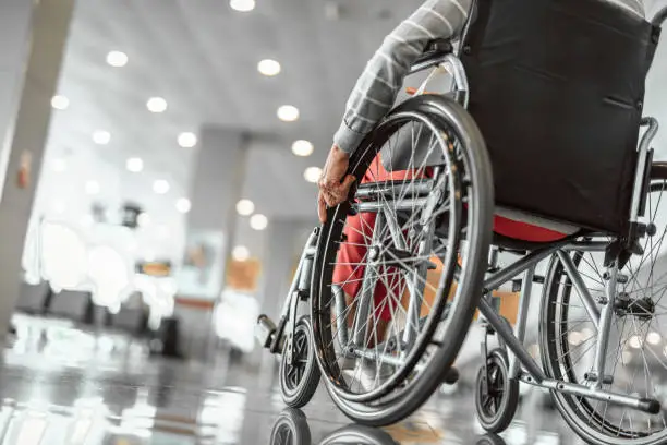 Cropped photo of mature female on wheelchair in the lobby at airport hall. Copy space in left side