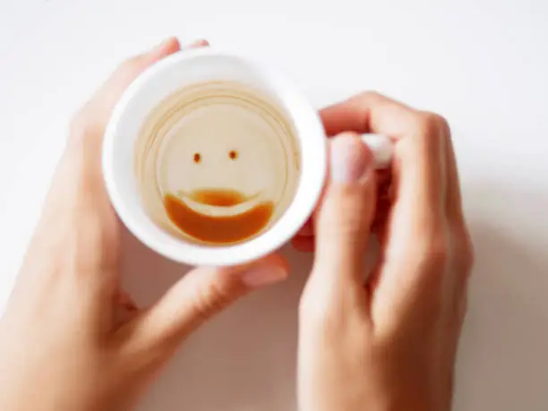 Empty coffee cup with smiling face. Womanholding white mug with coffee grinds. End of coffee break.