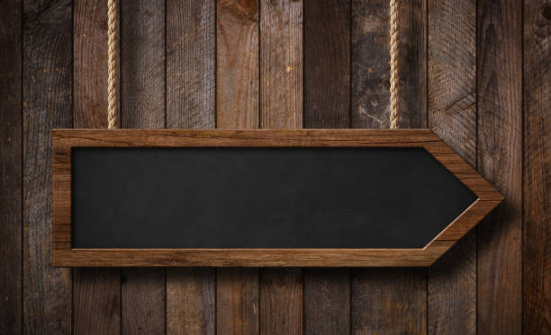 istock Arrow shaped blackboard hanging on ropes with wood planks background 1157453263