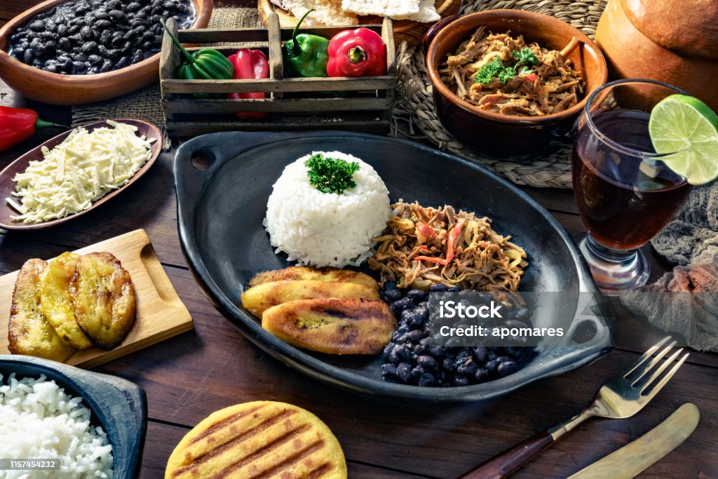 Venezuelan traditional food, Pabellon Criollo with arepas, casabe and papelon with lemon drink Venezuelan traditional food, Pabellon Criollo with arepas, casabe and papelon with lemon drink. Home made with white rice, black beans, fried plantains, and shredded beef. Plate on a wooden table in a rustic kitchen. Set with ingredients and shredded white cheese. Pabellon Criollo, is a main meal in the Venezuelan Culture and cuisine. Food Stock Photo