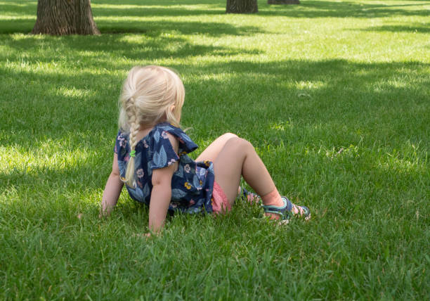 mała dziewczynka siedząca w zielonej trawie z zgiętymi kolanami - knees bent zdjęcia i obrazy z banku zdjęć