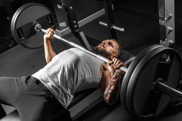 istock Bodybuilding. Bearded man lying doing bench press at gym with barbell making effort side view 1157459664