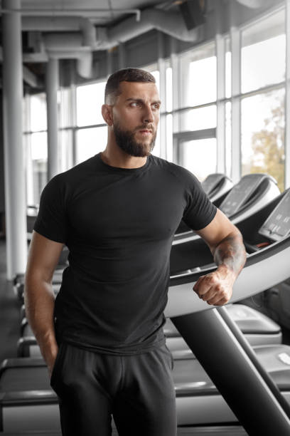 istock Professioal Occupation. Bearded trainer standing at gym leaning on treadmill pensive 1157459669