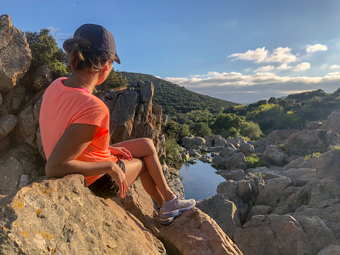 Young sport woman sitting on a rock and looking to the horizon in green mountain with waterfall river, peaceful meditation moment.