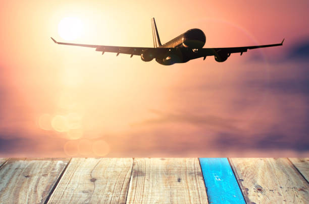 istock Airplane flying over tropical beach smooth wave and sunset sky abstract background. Copy space of empty old wood table business summer vacation and travel adventure concept. Vintage tone filter color. 1157475221