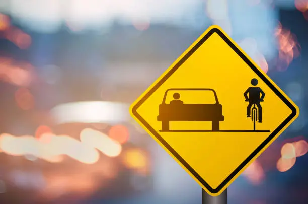 Bicycle and car share warning sign on blur traffic road with colorful bokeh light abstract background. Copy space of transportation and travel concept. Vintage tone filter color style.